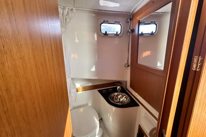 Slide: The Image of 2025 Sargo 31OB boat bathroom with wooden accents, compact sink, and porthole windows. - 41