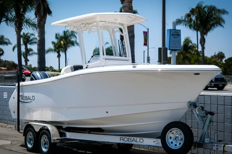 Slide: The Image of 2025 Robalo R230 Center Console boat on trailer, parked outdoors with palm trees. - 3