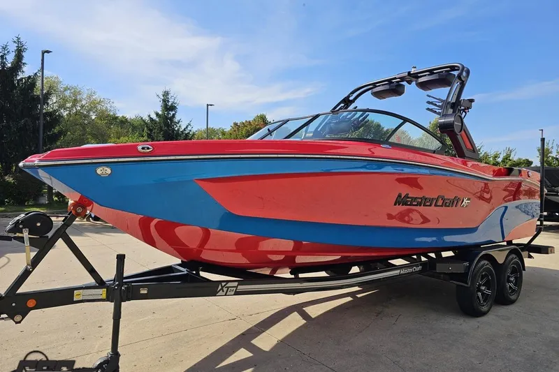 Slide: The Image of 2022 MasterCraft XT24 boat in vibrant red and blue on a trailer, outdoors. - 18