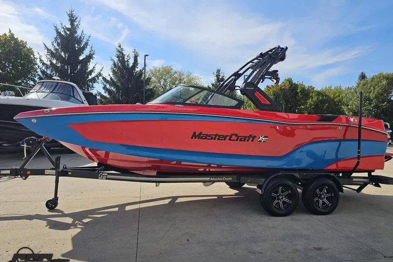 Slide: The Image of 2022 MasterCraft XT24 boat in vibrant red and blue on a trailer, outdoors. - 19