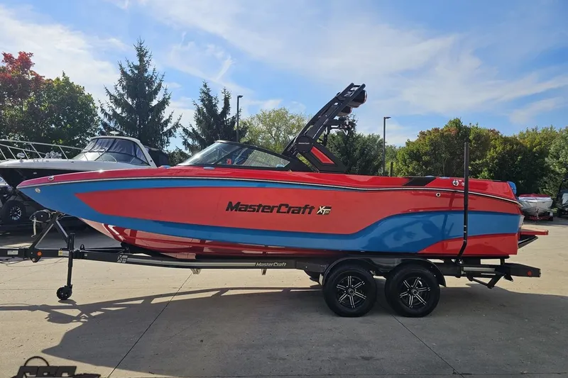 Slide: The Image of 2022 MasterCraft XT24 boat in vibrant red and blue on a trailer, outdoors. - 20