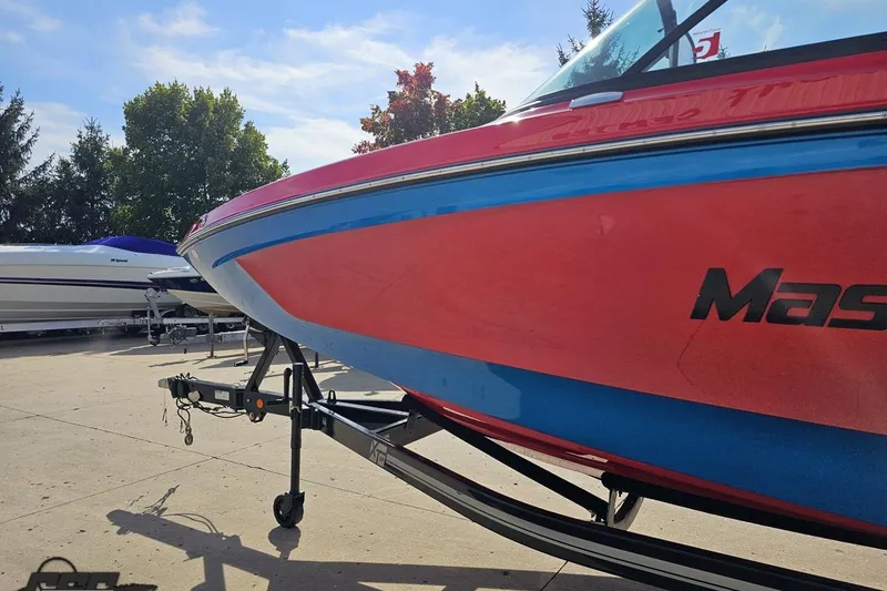 Slide: The Image of 2022 MasterCraft XT24 boat on trailer, vibrant red and blue design, parked outdoors. - 22