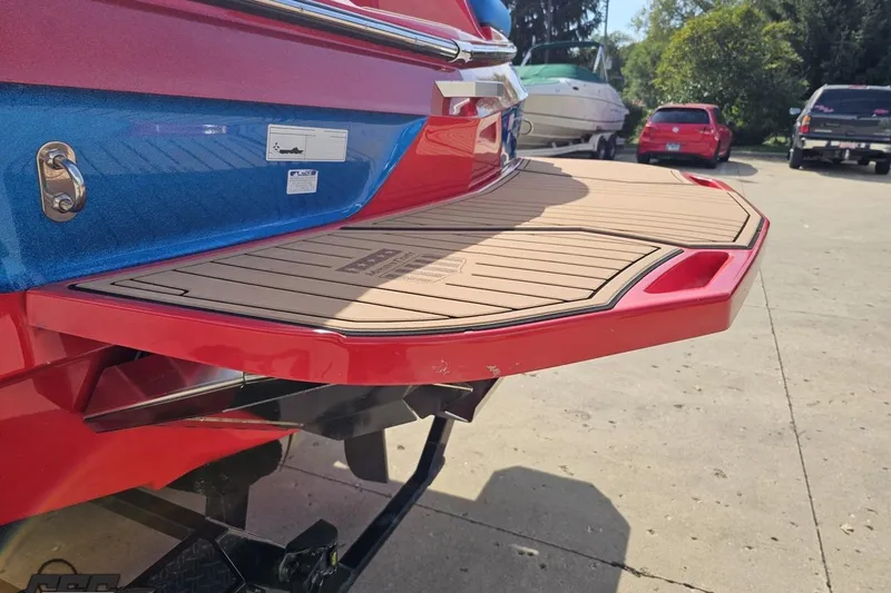 Slide: The Image of 2022 MasterCraft XT24 boat with red and blue detailing, featuring a teak swim platform. - 25
