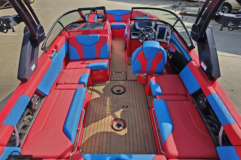 Slide: The Image of 2022 MasterCraft XT24 boat interior with red and blue seating, modern dashboard, and wood flooring. - 45