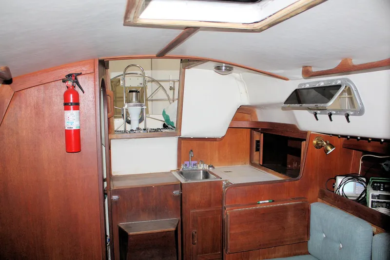 Slide: The Image of Interior of a 1986 J Boats J/28 sailboat, featuring a compact kitchen and wooden cabinetry. - 33