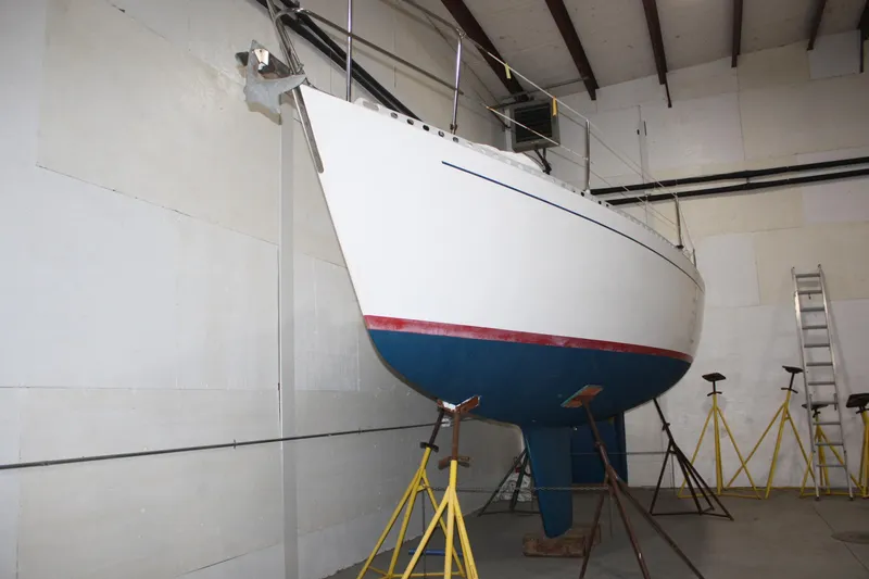 Slide: The Image of 1986 J Boats J/28 sailboat in storage, supported by stands, with a white and blue hull. - 7