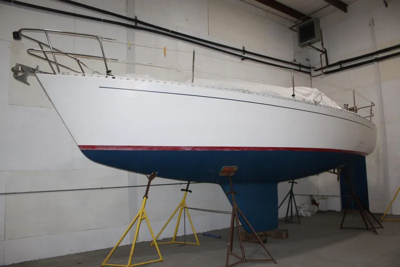 Slide: The Image of 1986 J Boats J/28 sailboat in storage, supported by stands, with a blue hull and white deck. - 8