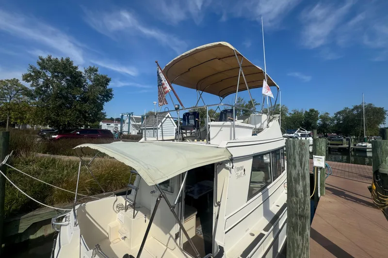 Slide: The Image of 1998 Camano Troll 31 boat docked, featuring a canopy and American flag, under a clear blue sky. - 56
