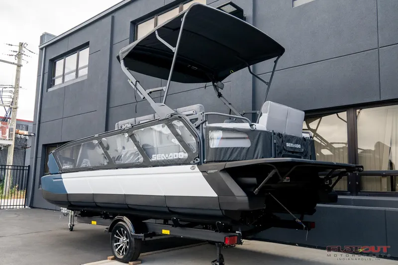 Slide: The Image of 2024 Sea-Doo Switch SPORT 21 230HP pontoon boat on trailer, parked outside building. - 1