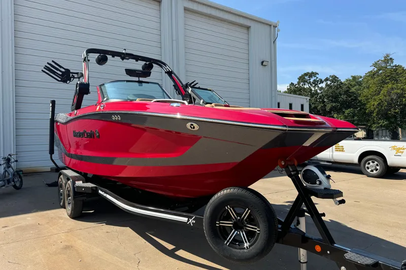 Slide: The Image of 2022 MasterCraft X24 boat in vibrant red on a trailer, parked outside a garage. - 2