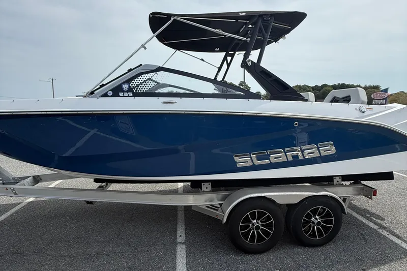 Slide: The Image of 2025 Scarab 235SE boat on trailer, blue and white design, parked outdoors. - 5