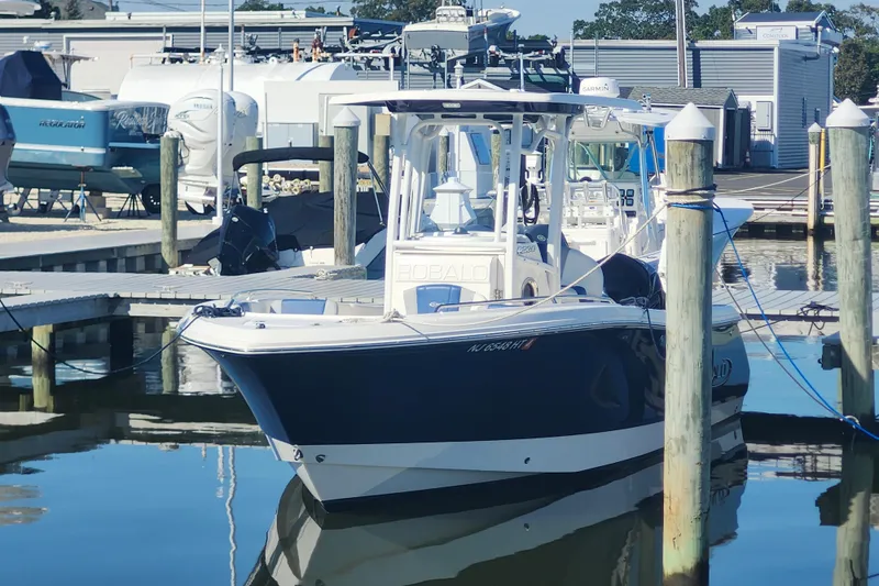 Slide: The Image of 2023 Robalo R230 Center Console boat docked at marina, reflecting on calm water. - 1