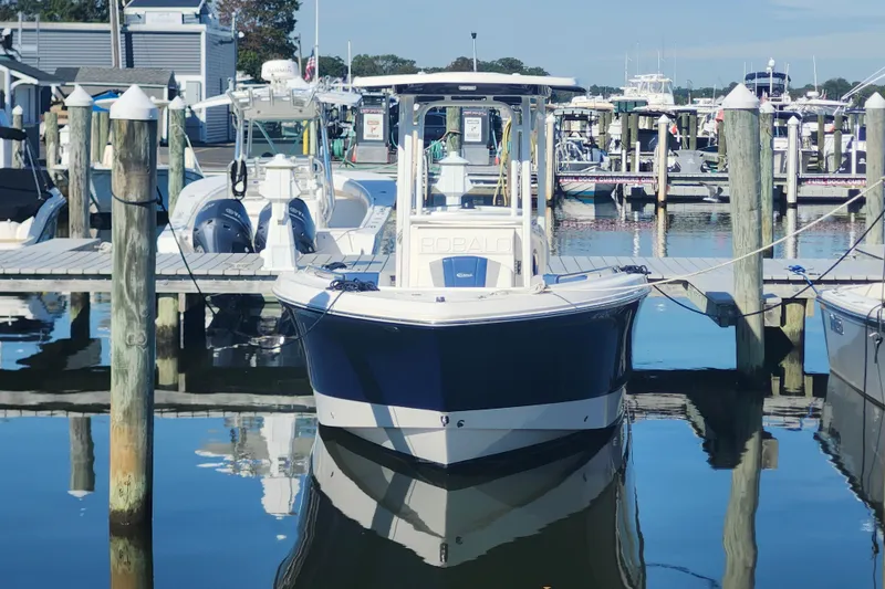 Slide: The Image of 2023 Robalo R230 Center Console boat docked at a marina, reflecting on calm water. - 2