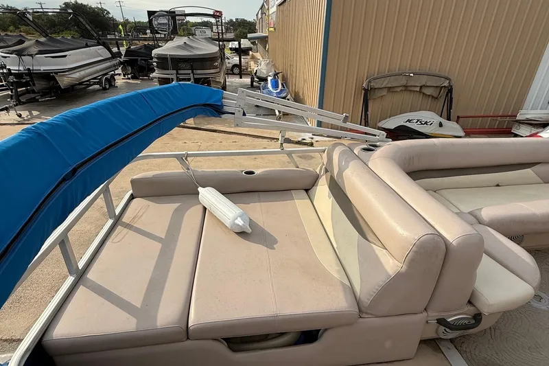 Slide: The Image of 2014 Sun Tracker Party Barge 22 DLX with beige seating and blue cover in a boatyard. - 9