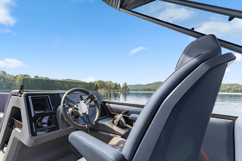 Slide: The Image of 2024 Manitou 22 Explore Max Bench boat interior with steering wheel, lake view, and clear sky. - 11