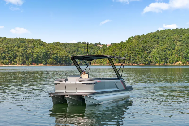 Slide: The Image of 2024 Manitou 22 EXPLORE MAX BENCH pontoon boat on a serene lake. - 2