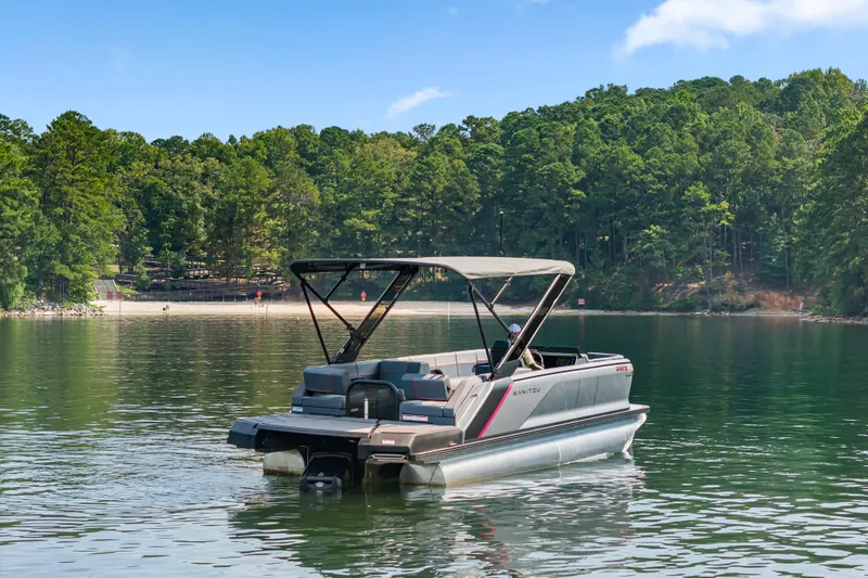 Slide: The Image of 2024 Manitou 22 Explore Max Bench pontoon boat on a serene lake with forested background. - 4