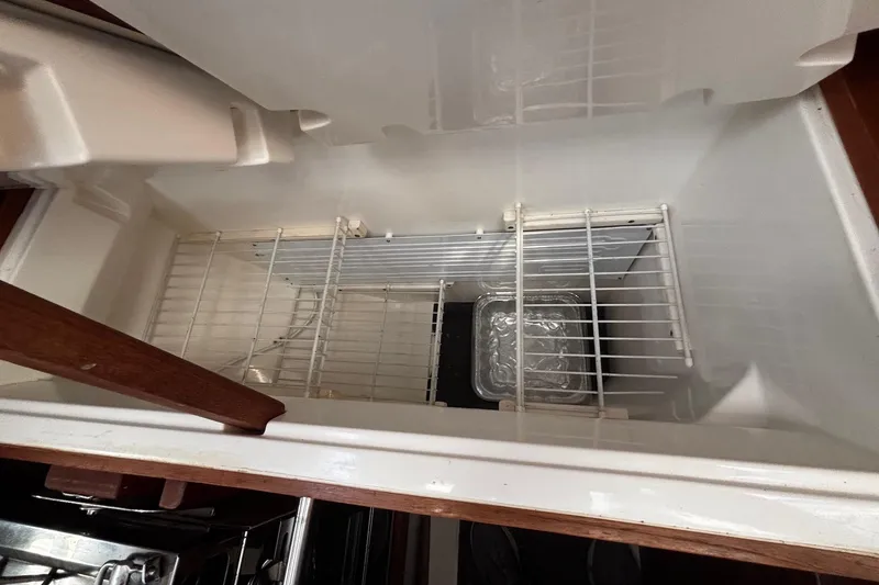 Slide: The Image of Empty refrigerator compartment in a 1993 Hunter 33.5 boat, featuring wire shelves and a tray. - 19