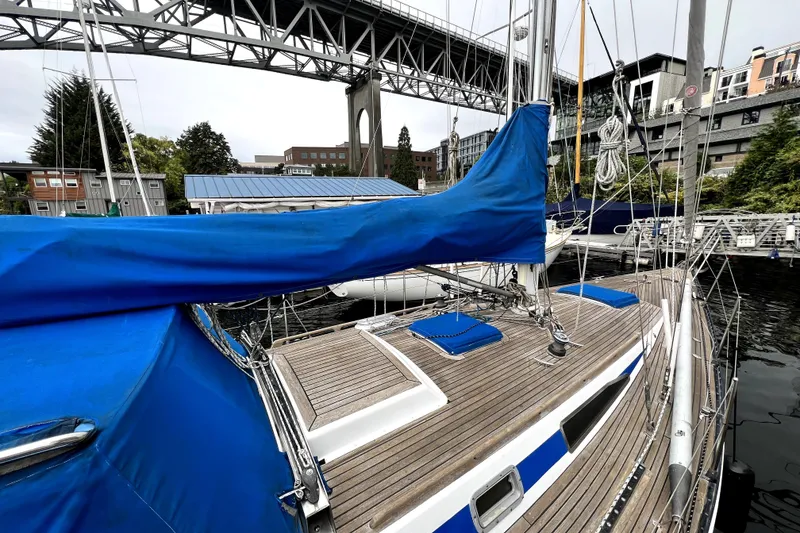 Slide: The Image of 1983 CT 38 Warwick sailboat docked under a bridge, featuring blue covers and wooden deck. - 2
