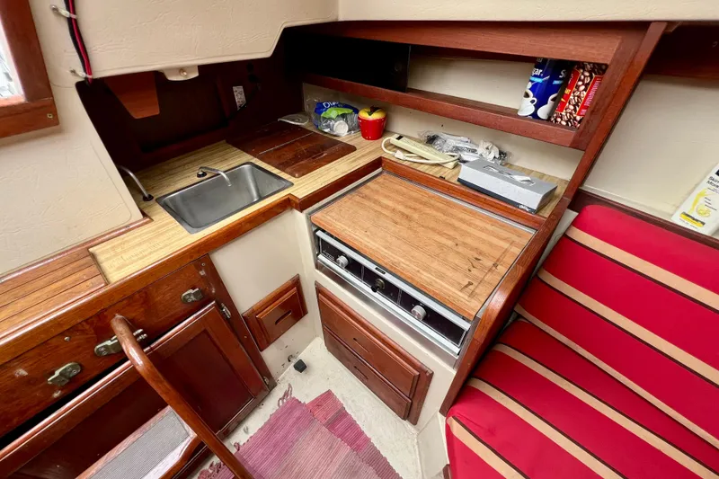 Slide: The Image of Interior of 1985 Catalina 27 sailboat kitchen with sink, stove, and red-striped seating. - 15
