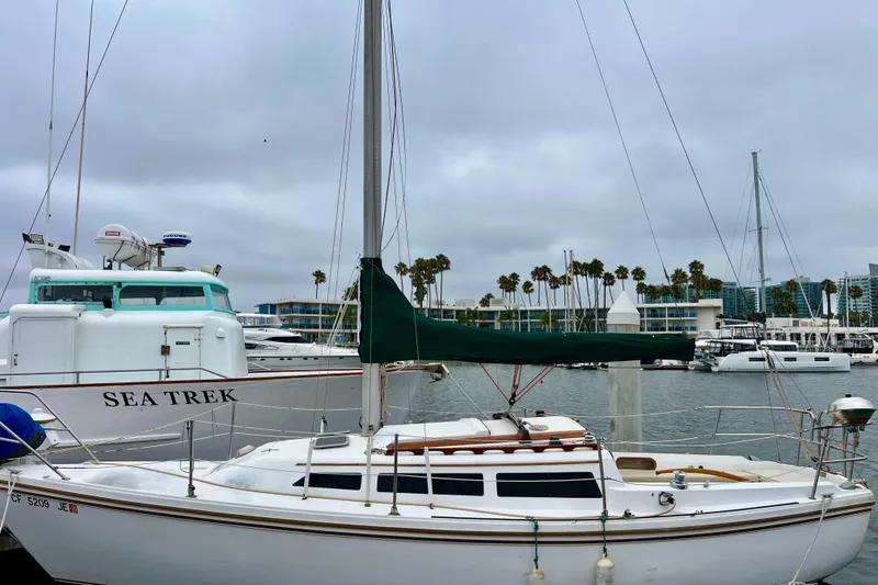 Slide: The Image of 1985 Catalina 27 sailboat docked in marina, overcast sky, palm trees in background. - 4