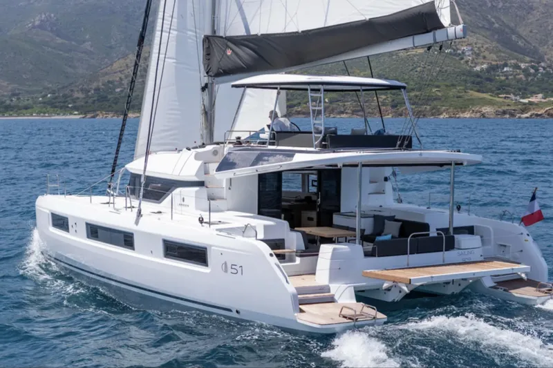 The Image of 2026 Lagoon 51 ICONIC catamaran sailing on the ocean with scenic coastal backdrop. - 1
