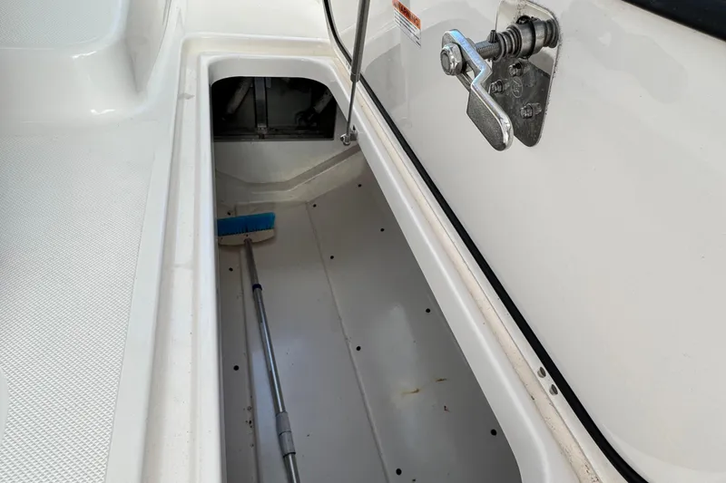 Slide: The Image of Storage compartment of a 2015 Pursuit DC 265 Dual Console boat with a broom inside. - 32