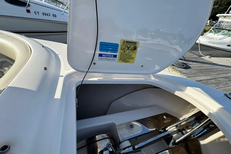 Slide: The Image of 2015 Pursuit DC 265 Dual Console boat storage compartment with open hatch and warning labels. - 45