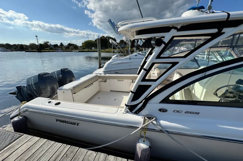 Slide: The Image of 2015 Pursuit DC 265 Dual Console boat docked by the water on a sunny day. - 5