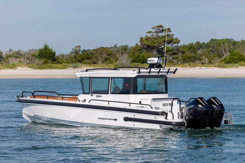 Slide: The Image of 2024 Axopar 28 CABIN boat cruising on water near a sandy shoreline. - 2