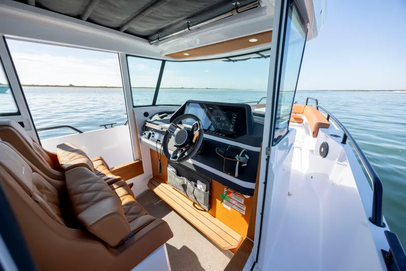 Slide: The Image of 2024 Axopar 28 CABIN interior with modern dashboard and leather seating on calm water. - 21