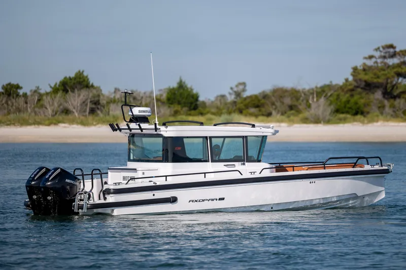 Slide: The Image of 2024 Axopar 28 CABIN boat cruising on calm water near a sandy shoreline. - 4