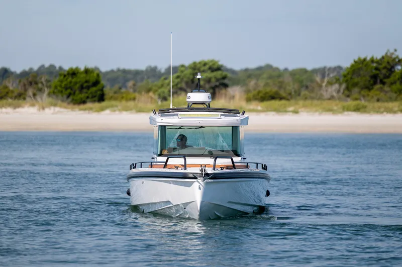 Slide: The Image of 2024 Axopar 28 CABIN boat cruising on calm water near a sandy shoreline. - 5