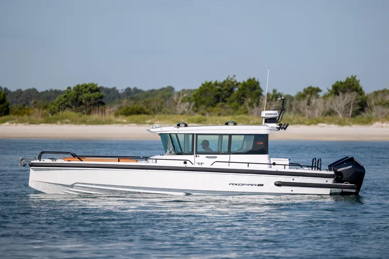 Slide: The Image of 2024 Axopar 28 CABIN boat cruising on calm water near a scenic shoreline. - 6