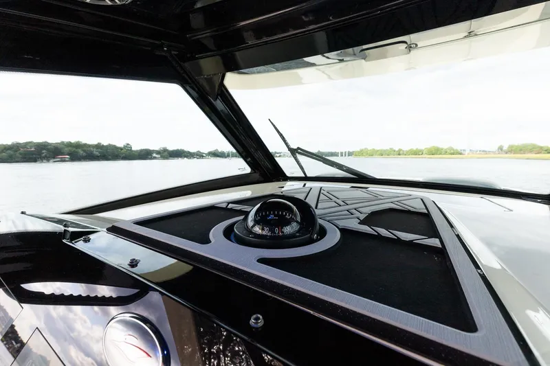 Slide: The Image of 2024 Scout 377 LXF boat dashboard with compass, overlooking serene water and lush shoreline. - 35
