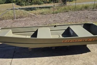 Slide: The Image of 2026 Tracker Grizzly 12 Jon boat on concrete, outdoors, with grassy background. - 2