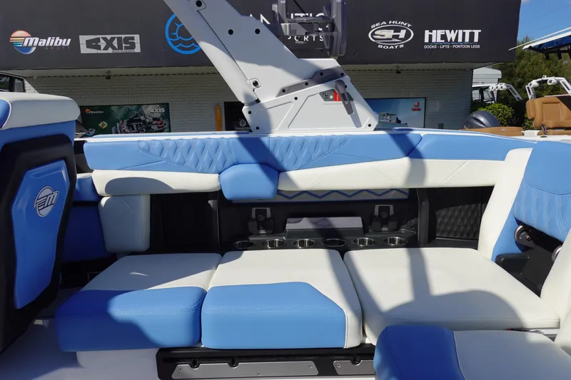 Slide: The Image of 2025 Malibu M230 boat interior with blue and white seating, cup holders, and branded logos. - 27