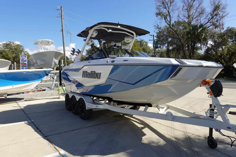 Slide: The Image of 2025 Malibu M230 boat on trailer, sleek design, parked outdoors under clear sky. - 3