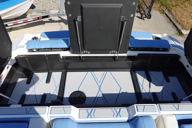 Slide: The Image of 2025 Malibu M230 boat interior storage compartment with blue accents and open hatch. - 44
