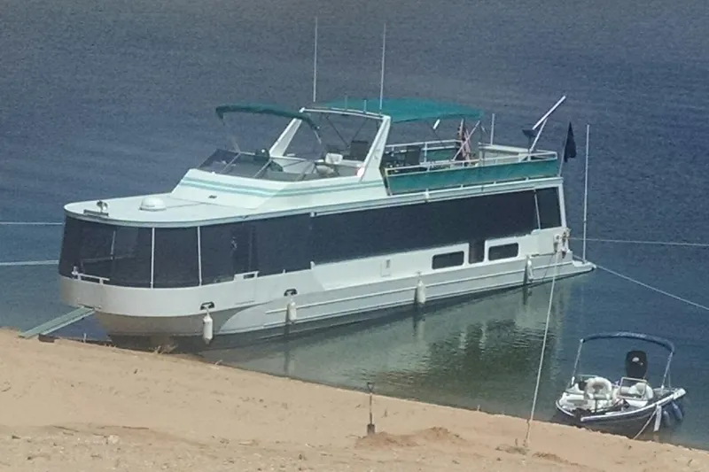The Image of 1993 Skipper Liner houseboat docked on calm water with a small boat nearby. - 0