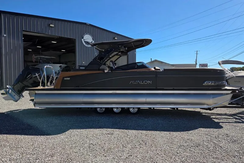Slide: The Image of 2026 Avalon Platinum Catalina 2785 Elite Windshield pontoon boat parked outside a warehouse. - 4