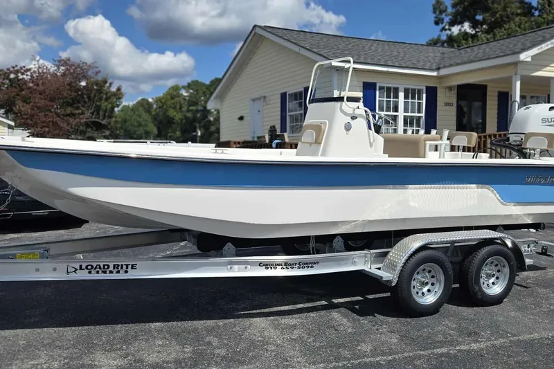 Slide: The Image of 2026 Sundance B22CCR boat on Load Rite trailer, parked outside a house under a cloudy sky. - 3