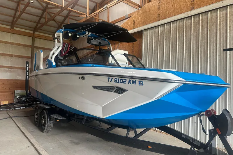 The Image of 2021 Nautique Super Air Nautique G25 boat in storage, blue and white exterior. - 1