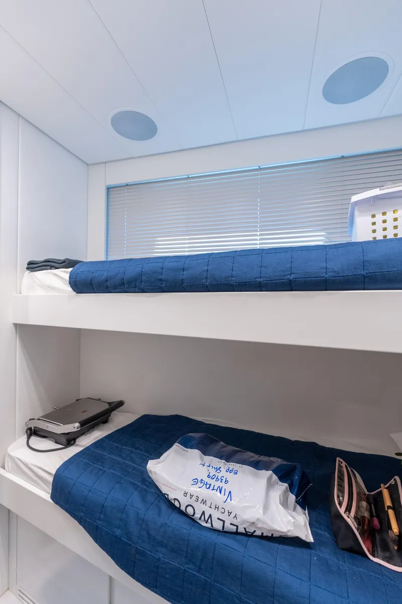 Slide: The Image of Bunk beds in a 2021 Pershing 9X yacht cabin with blue bedding and personal items. - 38