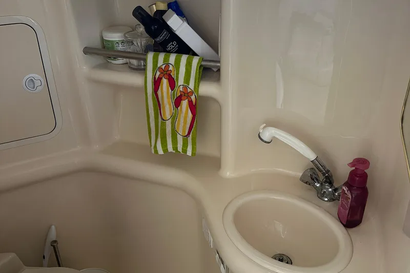Slide: The Image of Bathroom sink area in a 2000 Sea Ray 310 Sundancer boat, featuring toiletries and a colorful towel. - 18