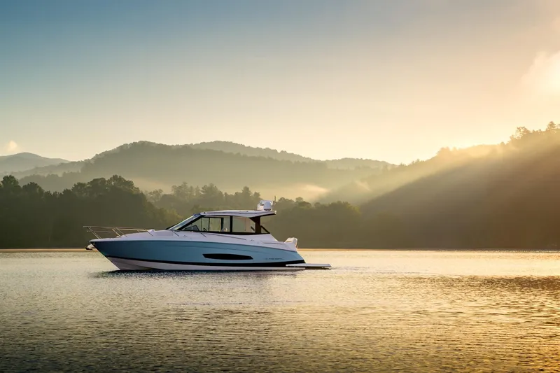 Slide: The Image of 2026 Regal 36 Grande Coupe yacht on serene lake at sunrise, surrounded by misty hills. - 25