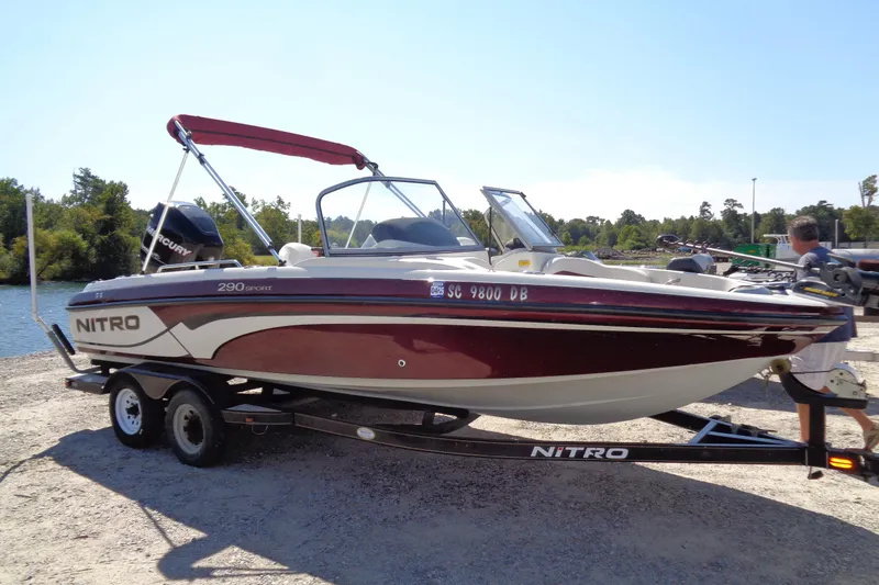 Slide: The Image of 2011 Nitro 290 boat on trailer, red and white, parked near water. - 3