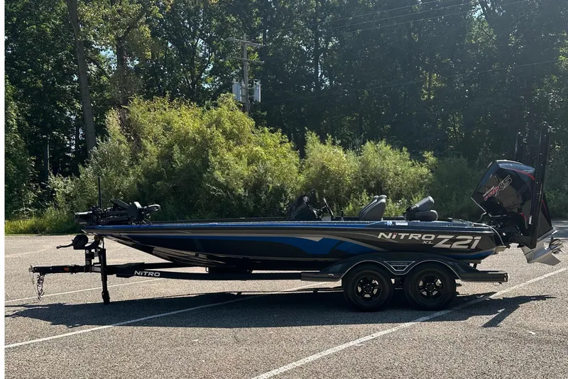 Slide: The Image of 2024 Nitro Z21 XL boat parked in a lot, surrounded by trees. - 2