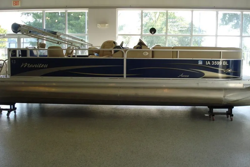 Slide: The Image of 2013 Manitou Aurora 22 VP pontoon boat displayed indoors, featuring blue and beige design. - 4