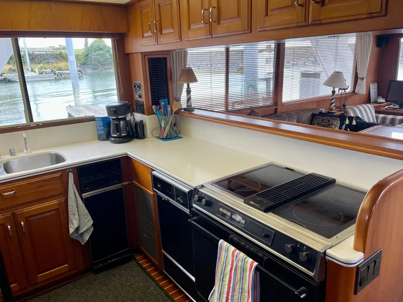Slide: The Image of 1987 Tollycraft Pilothouse Motor Yacht kitchen with stove, sink, and large windows overlooking water. - 11